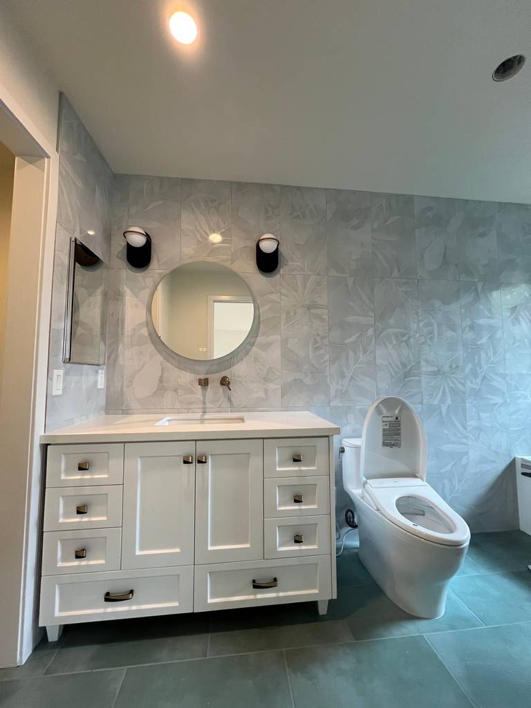 This bathroom features a modern white shaker vanity with integrated sink and wall-mounted round mirror.