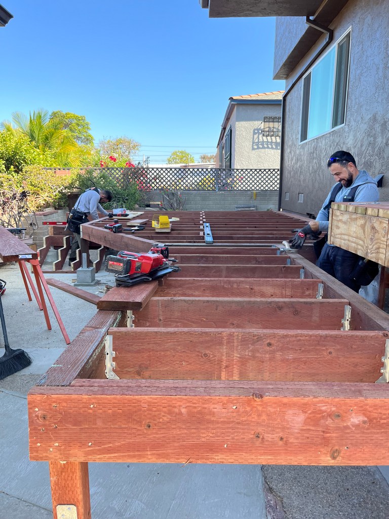 Contractors installing pressure-treated deck joists with joist hangers