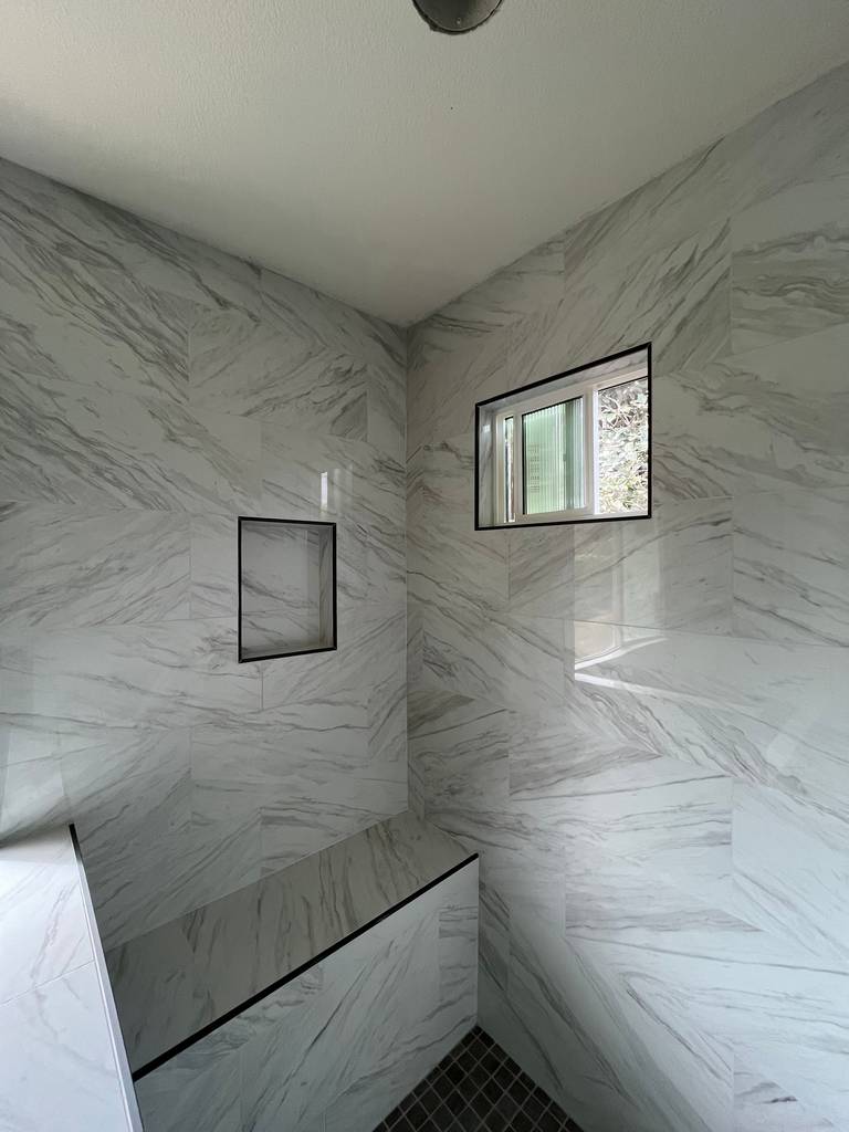Floor to ceiling marble tiles in bathroom with shower seat and niche